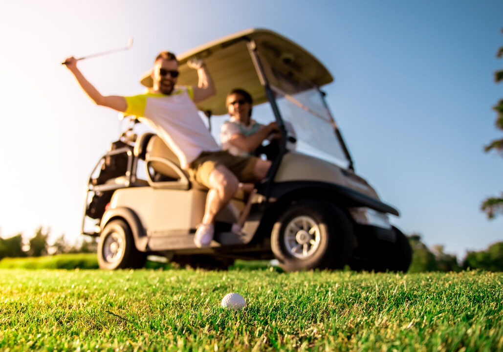 Golfer swinging club from golf cart at golf ball